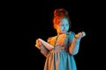 New device. Portrait of cute redheaded little girl wearing festive dress using tablet isolated over dark background in