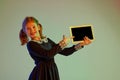 Portrait of cute redheaded little girl wearing festive dress using tablet isolated over light background in neon light