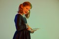 Portrait of cute redheaded little girl wearing festive dress using tablet isolated over light background in neon light