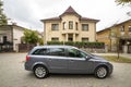 New expensive gray car parked in paved parking lot in front of big two story cottage. Luxury and prosperity concept