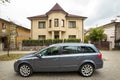 New expensive gray car parked in paved parking lot in front of big two story cottage. Luxury and prosperity concept