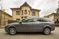 New expensive gray car parked in paved parking lot in front of big two story cottage. Luxury and prosperity concept