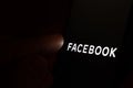 New Facebook company logo on the dark screen and finger about to touch it. Conceptual photo
