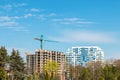 New finished residential building and one in construction with a crane by over blue sky in front of park with green trees in Royalty Free Stock Photo