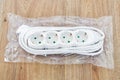 New four outlets power extension cord in a transparent plastic pakage on a wooden surface. White electric power strip for home or