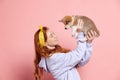 Cheerful redhead young girl with long curly hair holding cute little puppy of corgi dog isolated on pink background