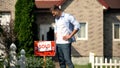 New house owner looking at sold signboard in front of house, dreams come true