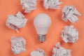 New idea concept with crumpled office paper and white light bulb on orange background. Creative solution during brainstorming. Royalty Free Stock Photo