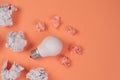 New idea concept with crumpled office paper and white light bulb on orange background. Creative solution during brainstorming Royalty Free Stock Photo