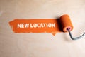 New Location. Paint roller with orange paint on a wooden surface