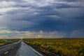 New Mexico scrub sage on rainy day with small fire with smoke beside the road and wet pavement to horizon with colored clouds