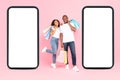New mobile shopping app. Excited black couple standing near huge cellphones with empty screens, holding shopper bags