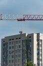 A new multi-storey house and a construction tower crane, illuminated by the sun against the background of a blue sk Royalty Free Stock Photo