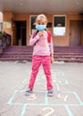 Back to school. A girl in mask jumping and playing hopscotch before school building Royalty Free Stock Photo