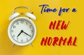 The new normal after COVID-19 Coronavirus pandemic concept. white alarm clock isolated on yellow with text time for a new normal