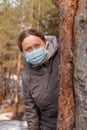 new normal the elderly, portrait happy elderly woman medical mask gray coat peeking out from behind a tree. Royalty Free Stock Photo