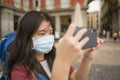 New normal holidays travel in Europe - young beautiful and happy Asian Chinese tourist woman with face mask and backpack taking Royalty Free Stock Photo