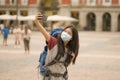 New normal holidays travel in Europe - young happy and beautiful Asian Korean tourist woman wearing mask taking selfie with mobile Royalty Free Stock Photo