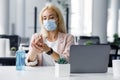 New normal and hygiene in office during coronavirus epidemic. Girl worker in protective mask with smart watch takes care