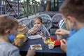New normal reality, stay safe in street cafe, father with kids in medical masks eating fast food