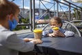 New normal reality, stay safe in street cafe, kids with medical mask waiting for breakfast Royalty Free Stock Photo