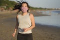 New normal running workout of Asian girl in face mask - young happy and beautiful Chinese woman jogging on the beach in post