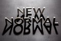 new normal word composed of silver metal letters on a flat matt black surface with shadows backlit