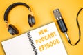 NEW PODCAST EPISODE text on notepad next to headphones and recording microphone