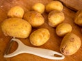 New potatoes and white peeler on a wooden worktop Royalty Free Stock Photo