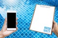 New smartphone with blank white paper on wooden clipboard over clear swimming pool water background Royalty Free Stock Photo