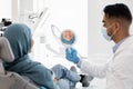 New Smile. Happy Islamic Lady Looking At Mirror While After Dental Treatment