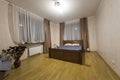 New spacious bedroom interior design in white and brown tone. Wooden floor and comfortable double bed, nice curtains on wide