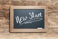 New Start Written on Slate Chalk Board Against Aged Wood Background