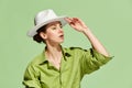 Portrait with serious young woman wearing white hat and touching headdress with hand over green background. New stylish Royalty Free Stock Photo
