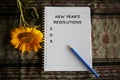New year resolution list concept on white notebook paper with yellow flower, notebook and pen.