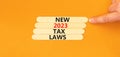 New 2023 tax laws symbol. Concept words New 2023 tax laws on wooden stick. Businessman hand. Beautiful orange table orange