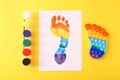 New trendy popular silicone colorful anti stress Pop It toy for child and colorful footprint on yellow background.