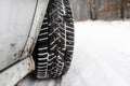 New winter tire in a silver car standing on a snow-covered road in the forest, a visible tread with snow. Royalty Free Stock Photo