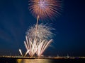 Bright fireworks burst in the blue sky with distant city lights and sea water Royalty Free Stock Photo