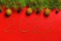 New Year 2022. Christmas banner made of fir branches with cones and balls on a red background. Beads inscription Royalty Free Stock Photo