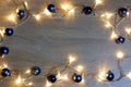 New year christmas frame from blue shiny and matte balls, christmas lights garland on light wood background copy space Royalty Free Stock Photo