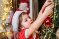 New year and Christmas kids concept. Christmas kid decorating Christmas tree with bauble. Little girl in santa hat Royalty Free Stock Photo