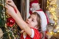 New year and Christmas kids concept. Christmas kid decorating Christmas tree with bauble. Little girl in santa hat Royalty Free Stock Photo