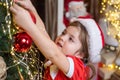 New year and Christmas kids concept. Christmas kid decorating Christmas tree with bauble. Little girl in santa hat Royalty Free Stock Photo