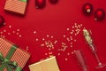 New Year Christmas presents, Christmas balls, champagne glasses, gold confetti stars on red background top view. Flat lay Xmas Royalty Free Stock Photo