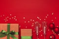 New Year Christmas presents, Christmas balls, champagne glasses, gold confetti stars on red background top view. Flat Royalty Free Stock Photo