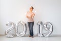 New 2019 Year is coming concept - Happy woman standing near silver colored numbers and sparklers indoors. Royalty Free Stock Photo