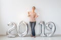 New 2019 Year is coming concept - Happy woman standing near silver colored numbers and sparklers indoors. Royalty Free Stock Photo