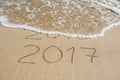 New Year 2017 is coming concept - inscription 2016 and 2017 on a beach sand, the wave is almost covering the digits 2016 Royalty Free Stock Photo