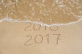 New Year 2017 is coming concept - inscription 2016 and 2017 on a beach sand, the wave is almost covering the digits 2016 Royalty Free Stock Photo